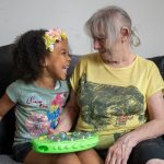 An older woman sitting next to and smiling at a young girl.