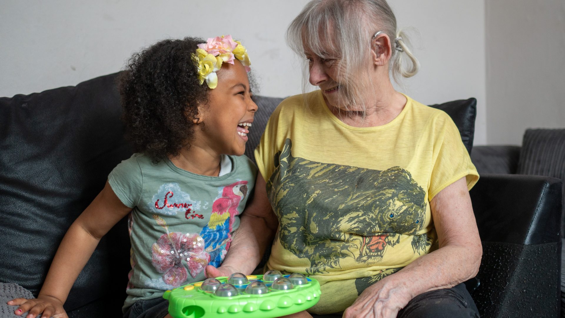 An older woman sitting next to and smiling at a young girl.