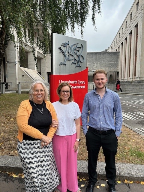 Three people standing next to each other outside the Welsh government buildings in Cardiff.  